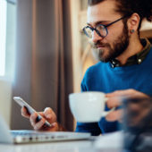 Mann arbeitet zuhause am Laptop und hat eine Kaffeetasse in der Hand.